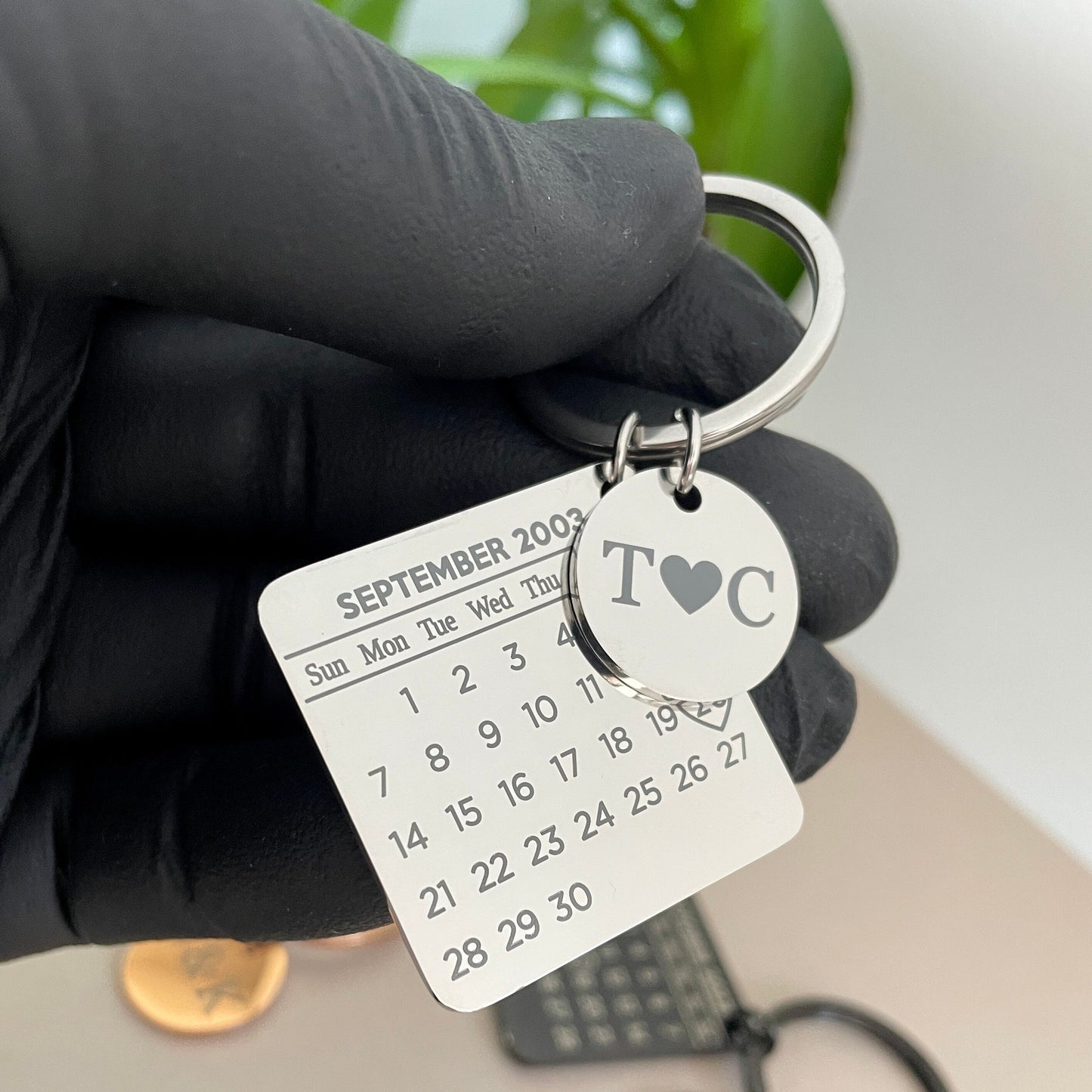 Zoom in on the laser-engraved detail of the keychain. Show how crisp and clear the DD/MM/YYYY date format and initials look on the stainless steel surface. This close-up emphasizes the quality craftsmanship and personal touch of the keychain.