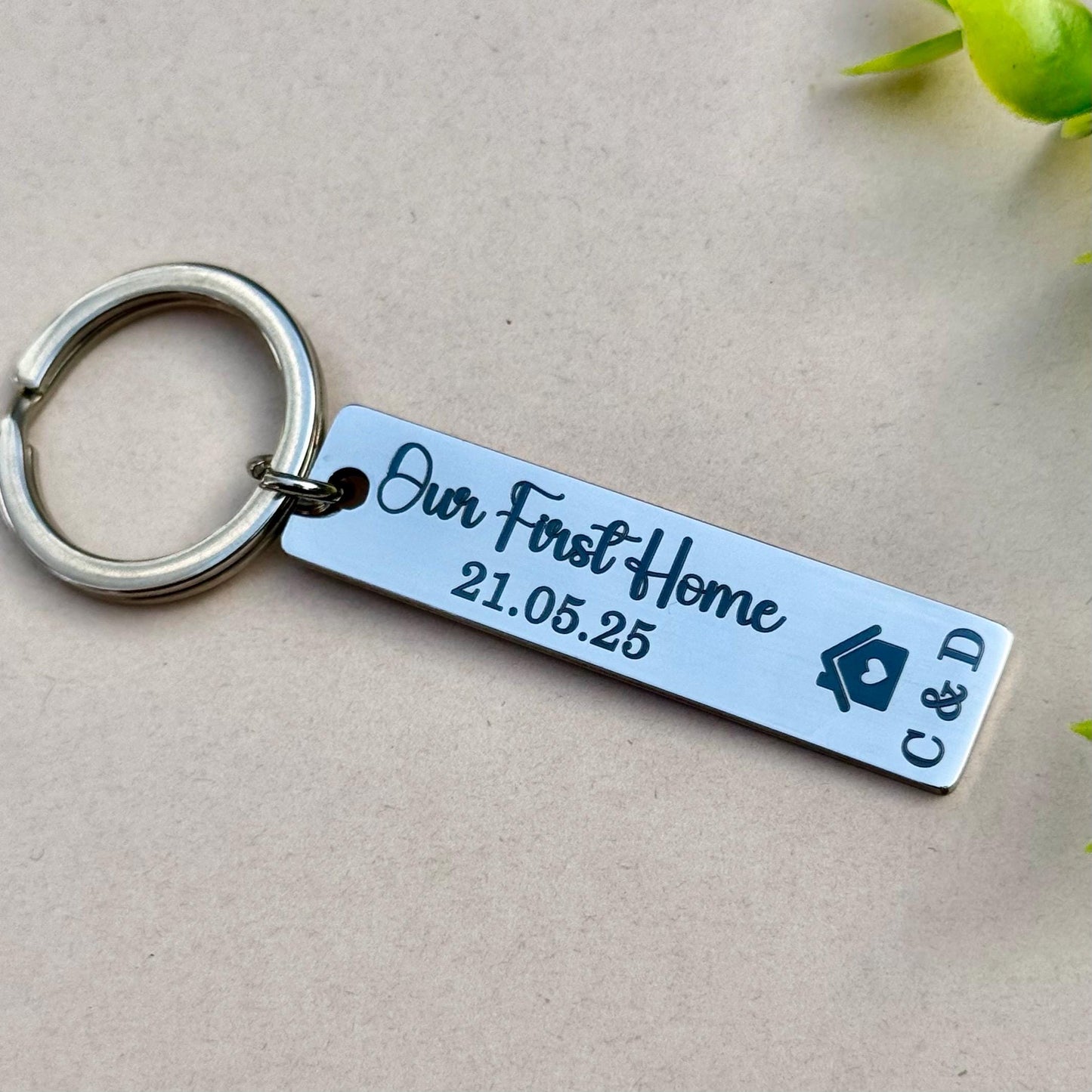 Personalized stainless steel keychain engraved with 'Our First Home 21.05.25' and the initials 'C&D,' along with a house symbol. This elegant and modern keychain makes a thoughtful gift for first-time homeowners or couples commemorating their new home. The high-quality stainless steel keychain features a sleek, polished finish and is attached to a durable metal ring, perfect for keys or as a keepsake.