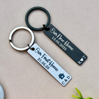 et of two personalized engraved stainless steel keychains, perfect for celebrating home milestones. The black keychain features &#39;Our New Home 13.05.2025&#39; and initials &#39;R.T.&#39; with a heart symbol, ideal for couples. The silver keychain is engraved with &#39;Our First Home 21.05.25&#39; and initials &#39;C.D.&#39; with a house symbol, making it a great gift for first-time homeowners. Both keychains are made from durable stainless steel, attached to sturdy metal rings, and feature a